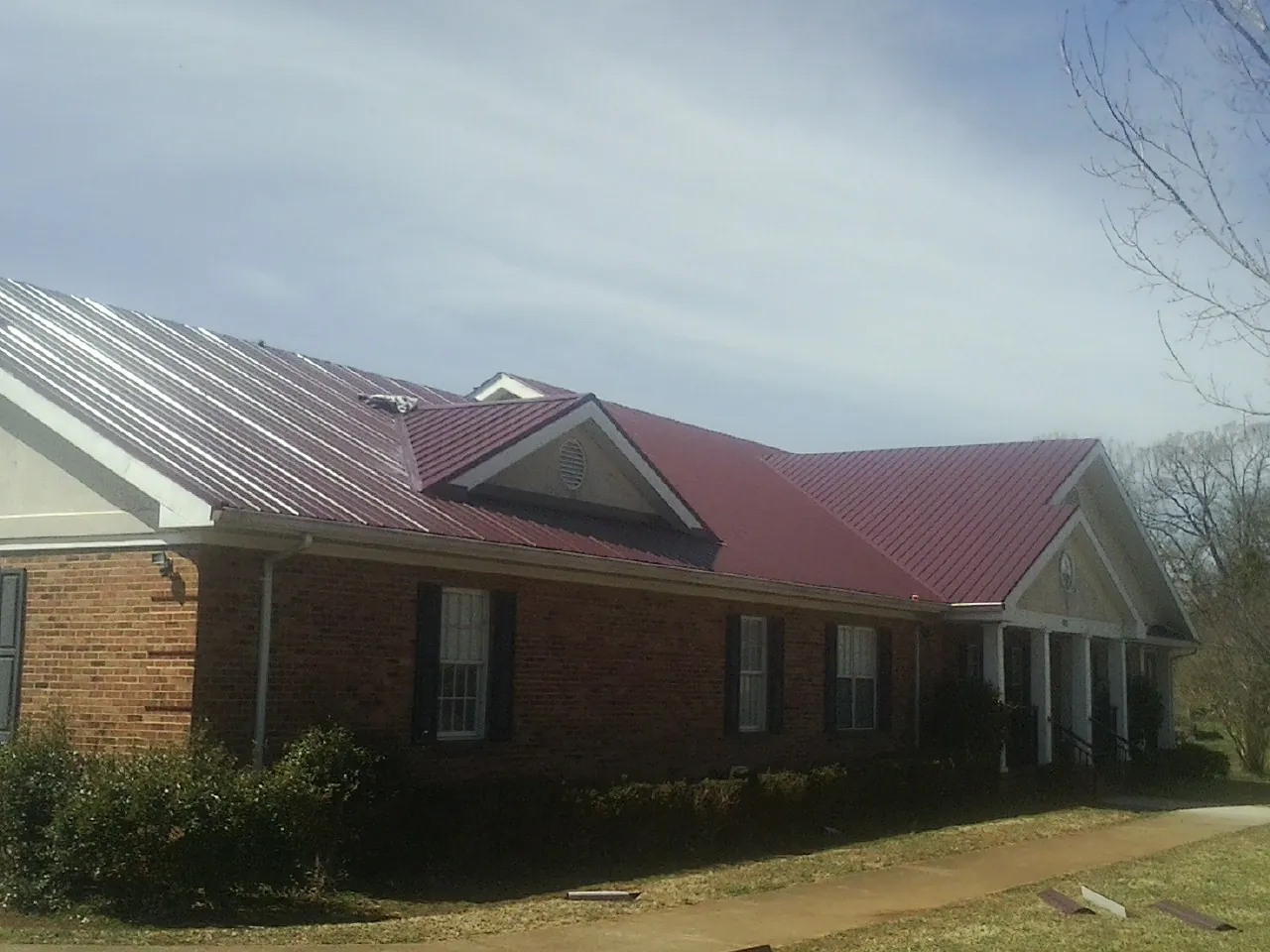 Red metal roof with gabled entries on a long brick building, from a Hail Damage Roof Repair job in Draper